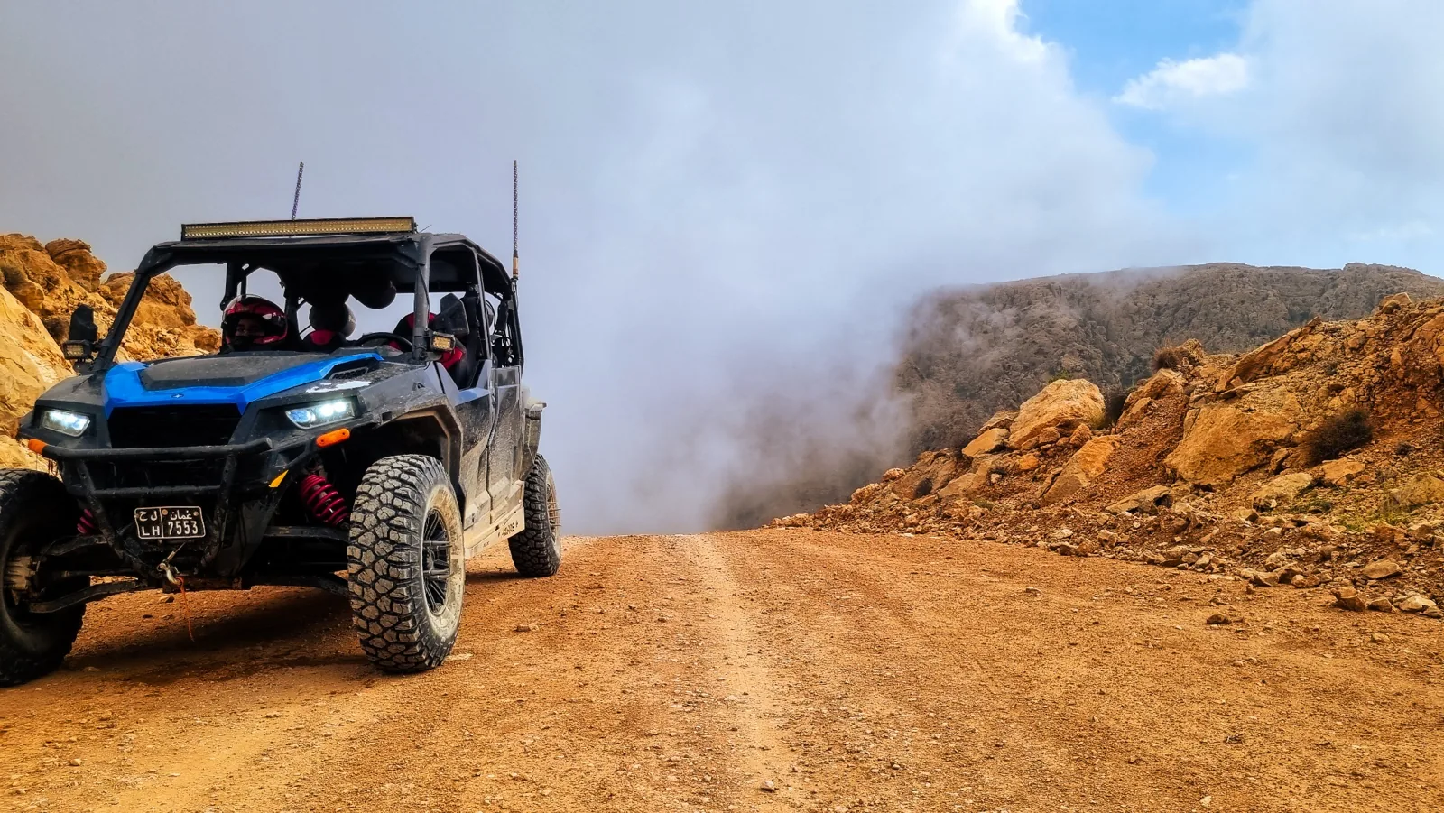 A side-by-side on a rocky mountain track beside low cloud