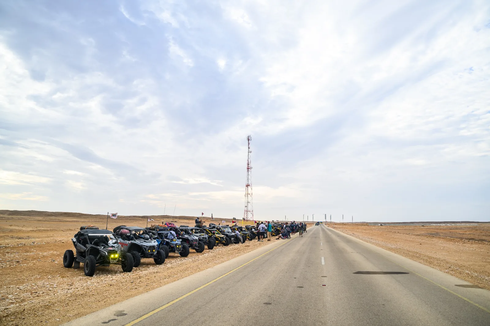 A long line of off-road vehicles gathered beside a road for a shared journey