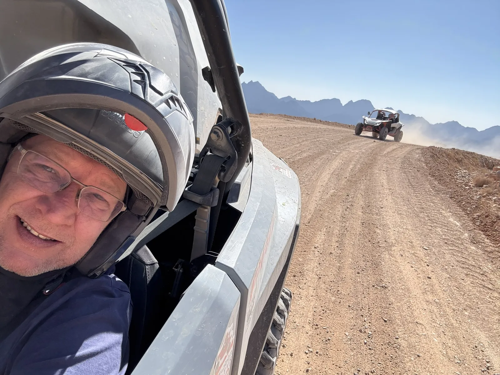 A helmeted guest in a UTV with another machine on the mountain trail behind