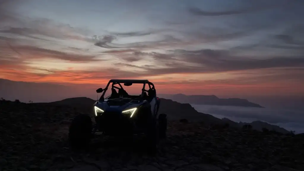 A UTV at a mountain sunset with clouds below the ridge