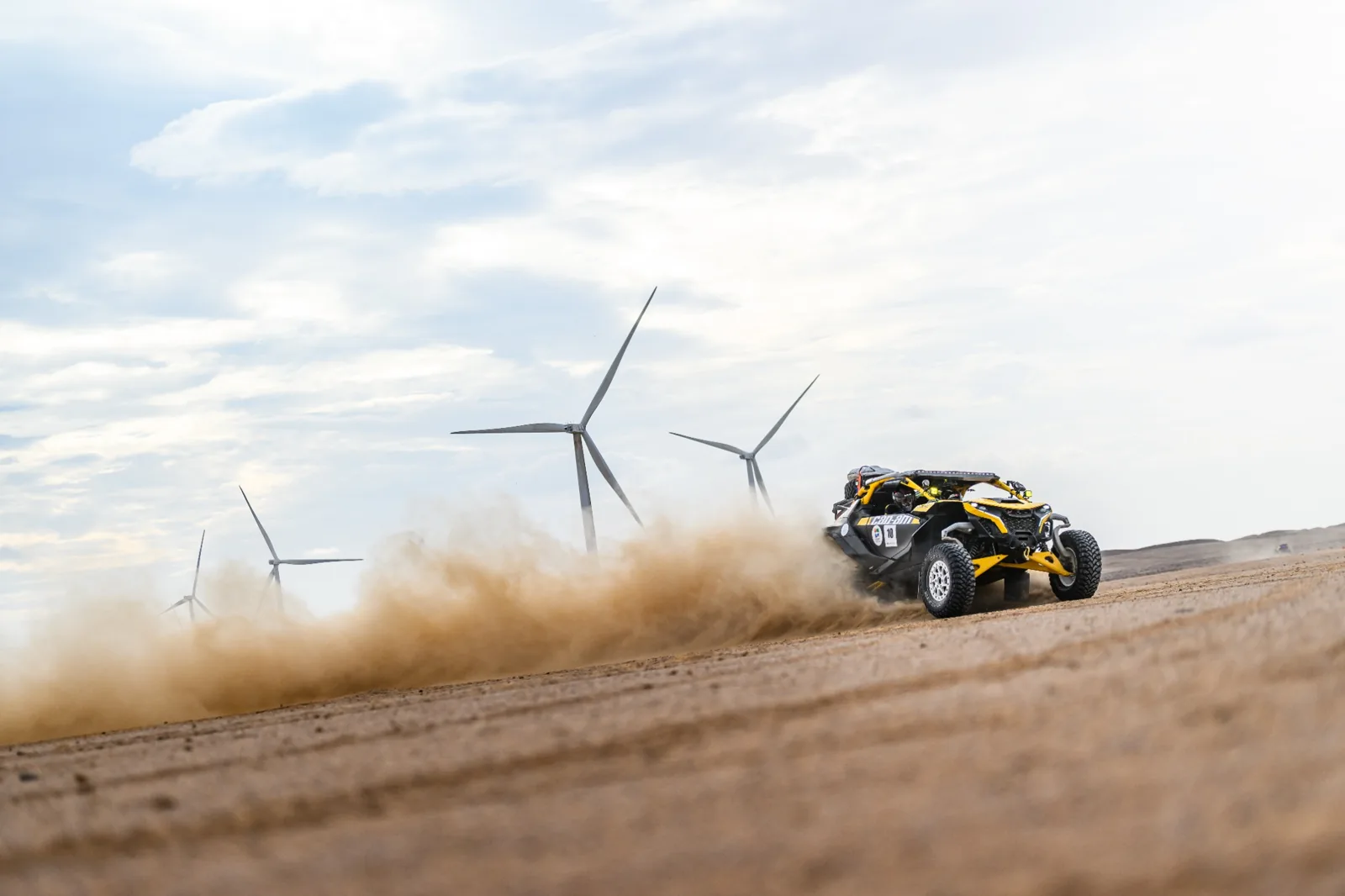 An off-road buggy crossing open terrain beside wind turbines in Oman