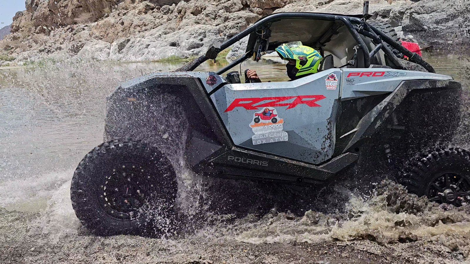 A FOX ATVs Polaris RZR splashes through clear wadi water on a guided expedition