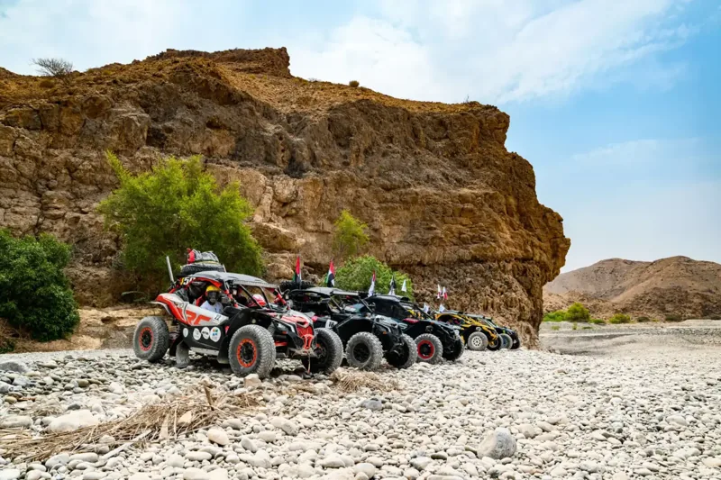 FOXATVs buggies carrying Omani flags beneath a wadi cliff